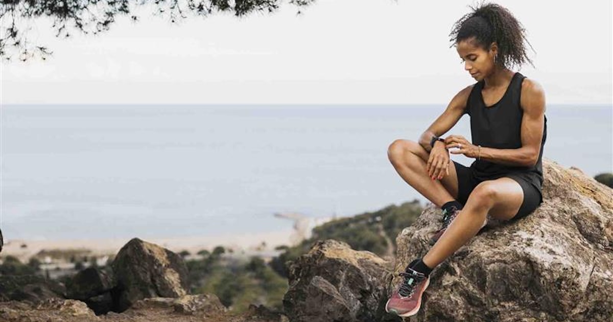 Runner sitting next to the ocean while looking at their smartwatch Runner sitting next to the ocean while looking at their smartwatch