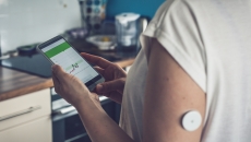 Person wearing a continuous glucose monitor and looking at a phone Person wearing a continuous glucose monitor and looking at a phone