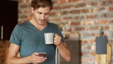 Person holding a cellphone and a cup of coffee Person holding a cellphone and a cup of coffee