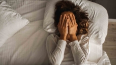 Person lying in bed with their hands over their eyes Person lying in bed with their hands over their eyes