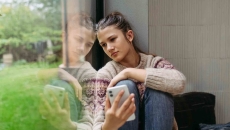 Person sitting by a window while holding a phone Person sitting by a window while holding a phone