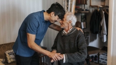 Two individuals with one in a wheelchair and the other standing over them with the two putting their heads together Two individuals with one in a wheelchair and the other standing over them with the two putting their heads together