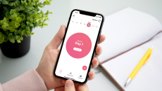 A person holding a smartphone displaying the app. The screen reads, "Period: Day 1." A person holding a smartphone displaying the app. The screen reads, "Period: Day 1."