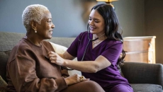 Healthcare provider sitting on a couch with a patient in their home checking their vitals. Healthcare provider sitting on a couch with a patient in their home checking their vitals.