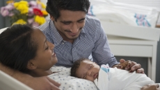 Two people, one lying in a hospital bed and the other leaning over the bed, with both looking at a baby Two people, one lying in a hospital bed and the other leaning over the bed, with both looking at a baby