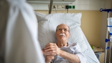 person in hospital bed holds hand of person in white lab coat person in hospital bed holds hand of person in white lab coat
