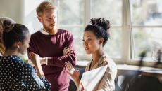 People standing in a circle with one of them holding a large piece of paper People standing in a circle with one of them holding a large piece of paper