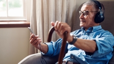 Person sitting in a chair while holding a phone and a cane and wearing headphones Person sitting in a chair while holding a phone and a cane and wearing headphones