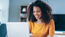 Person sitting at a table while looking at a computer and smiling Person sitting at a table while looking at a computer and smiling