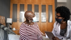 Two individuals sitting in a home looking at each other while wearing face masks Two individuals sitting in a home looking at each other while wearing face masks