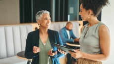 Two individuals walking in an office while another one is sitting in the background Two individuals walking in an office while another one is sitting in the background