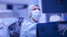 Healthcare provider wearing scrubs and a face mask while looking at a computer screen Healthcare provider wearing scrubs and a face mask while looking at a computer screen