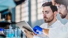 Two scientists in a laboratory setting looking at a piece of paper near some beakers Two scientists in a laboratory setting looking at a piece of paper near some beakers