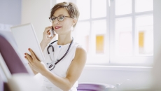 Healthcare provider wearing a stethoscope around their neck while looking at a tablet Healthcare provider wearing a stethoscope around their neck while looking at a tablet