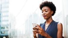Person standing outside while looking at a phone with the appearance of a city behind her