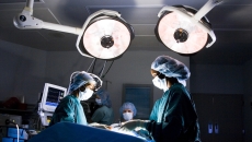 Surgeons in an operating room standing above a patient on a table with large lights above them Surgeons in an operating room standing above a patient on a table with large lights above them