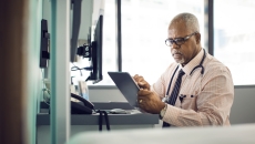 Healthcare provider sitting at a desk while looking at a tablet Healthcare provider sitting at a desk while looking at a tablet