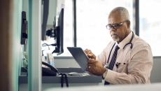 Physician sitting at their desk while looking at a tablet Physician sitting at their desk while looking at a tablet