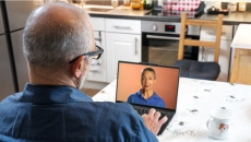 Person sitting at a table while looking at a computer with a person on it Person sitting at a table while looking at a computer with a person on it