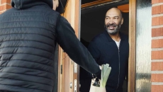 Person answering their front door and getting a delivery from another person Person answering their front door and getting a delivery from another person