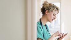 Healthcare provider in green scrubs wearing a stethoscope around their neck while looking at a tablet