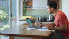 Person sitting at a table in a kitchen looking at their laptop Person sitting at a table in a kitchen looking at their laptop