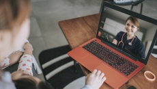 Person sitting down while looking at an orange and black laptop with a healthcare provider on the screen Person sitting down while looking at an orange and black laptop with a healthcare provider on the screen
