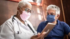 A doctor holding a tablet while talking to a patient.