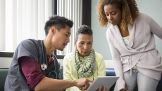 A doctor looking at data on a tablet with a patient and her family member. A doctor looking at data on a tablet with a patient and her family member.
