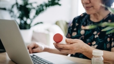 A person holding a pill bottle while using a laptop. A person holding a pill bottle while using a laptop.