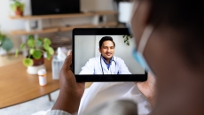 Person holding up a tablet with a telehealth provider on the screen Person holding up a tablet with a telehealth provider on the screen