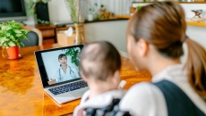 A mom holding a baby talking to a doctor via telehealth A mom holding a baby talking to a doctor via telehealth
