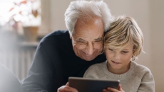 An older man and a child using a tablet together An older man and a child using a tablet together