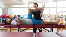 A male patient lying on his back on a massage table and a female physical therapist holding his leg up. A male patient lying on his back on a massage table and a female physical therapist holding his leg up.