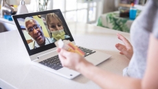A close up of a woman holding a bottle of pills while talking to two providers via telehealth