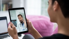 Person sitting in a room while holding a tablet that has a healthcare provider on the screen