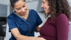 Healthcare professional listening to a pregnant person's stomach with a stethoscope