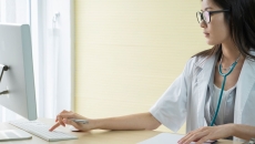 Healthcare provider sitting at a desk wearing a stethoscope around their neck and working on a computer