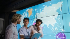 Three people standing in front of a screen showing continents connected by lines
