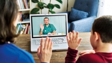 Two people waving at a healthcare provider on a computer
