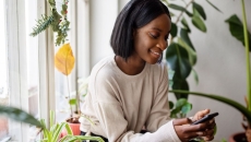 Person sitting in a chair and surrounded by plants while looking at a phone