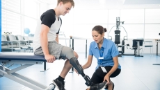 Person with a prosthetic leg undergoing physical therapy with a physical therapist beside them