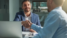 Two people sitting on opposite sides of a table while shaking hands