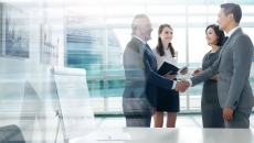 Four people in a room with two of them shaking hands while the other two watch