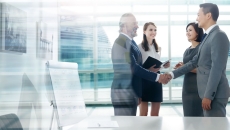 Two people shaking hands with two more people watching