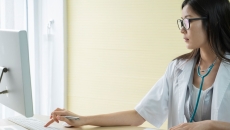 A doctor reviewing a patient's record in a desktop computer