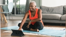 An older woman sitting on a yoga mat looking at exercises on her tablet An older woman sitting on a yoga mat looking at exercises on her tablet
