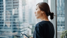 A young woman using a smartphone and looking out a window. A young woman using a smartphone and looking out a window.