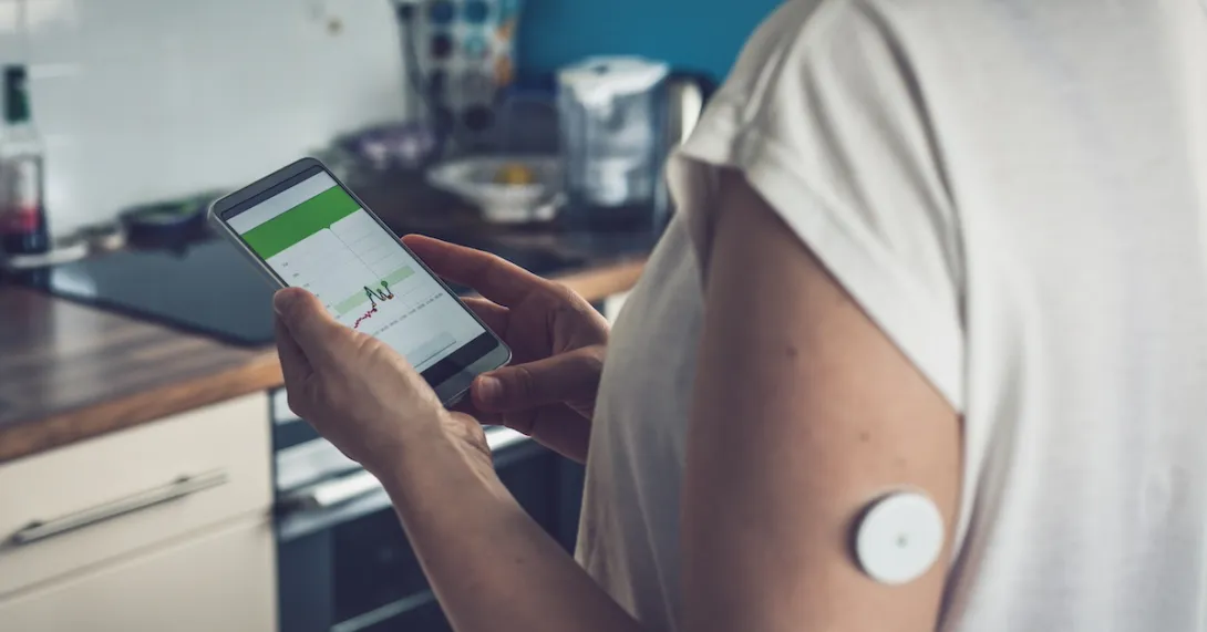 Person wearing a continuous glucose monitor and looking at a phone Person wearing a continuous glucose monitor and looking at a phone