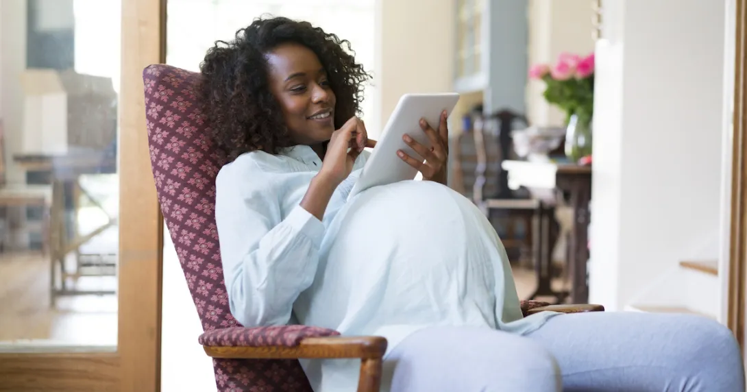 Pregnant person sitting in a chair looking at a tablet Pregnant person sitting in a chair looking at a tablet